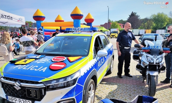 policjant stoi obok motocyklu, po lewej stronie stoi radiowóz