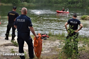 policjanci, strażacy i ratownicy stoją przy zbiorniku wodnym,na wodzie łódka